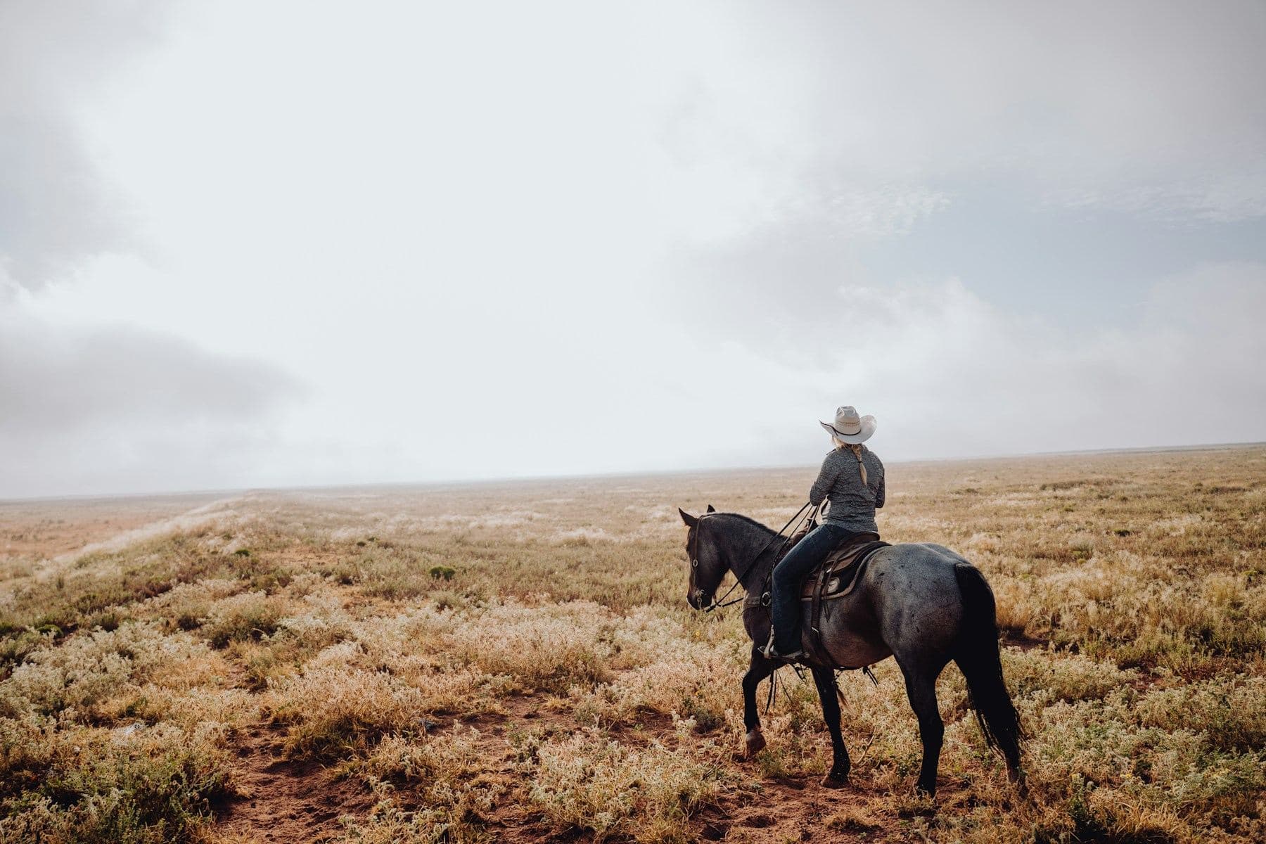 A rider on horseback crossing sagebrush country under a wide sky.